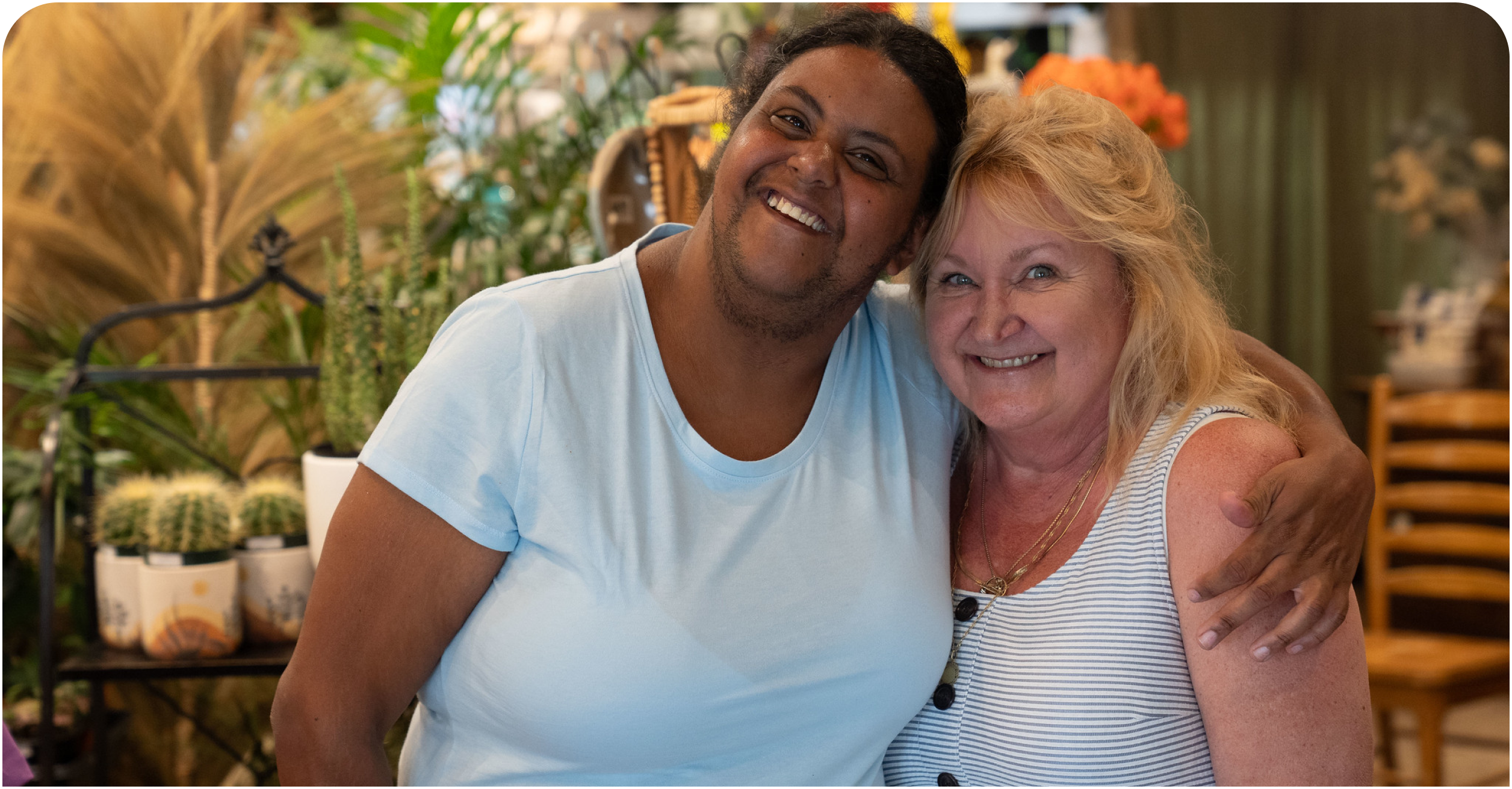 Two women hugging and smiling together with planets and greenery behind them