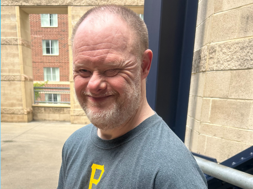 Middle aged man wearing a gray shirt smiling for the camera